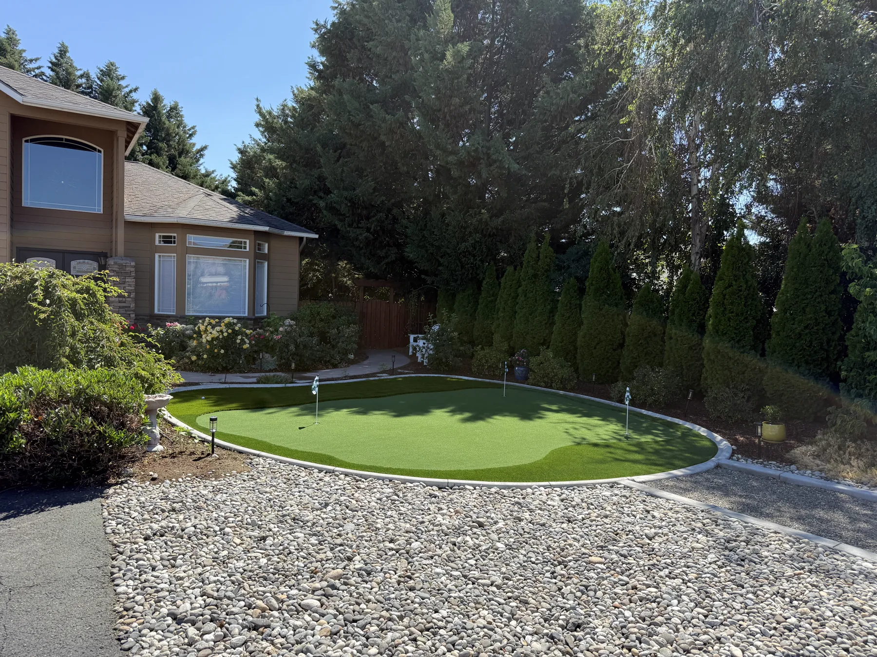 Front yard putting green framed by gravel and evergreen hedges