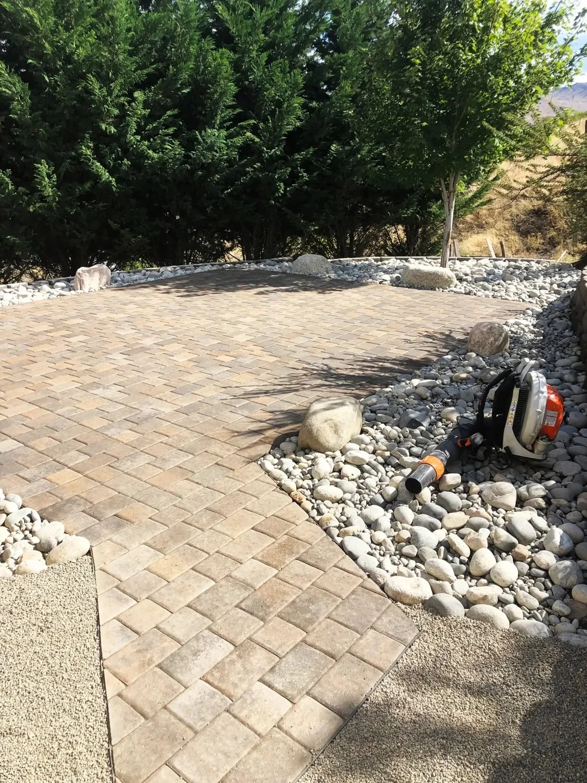 Interlocking paver patio edged with natural boulders and river rock