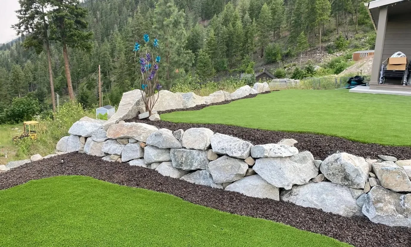 Two artificial turf lawn terraces divided by a natural boulder retaining wall