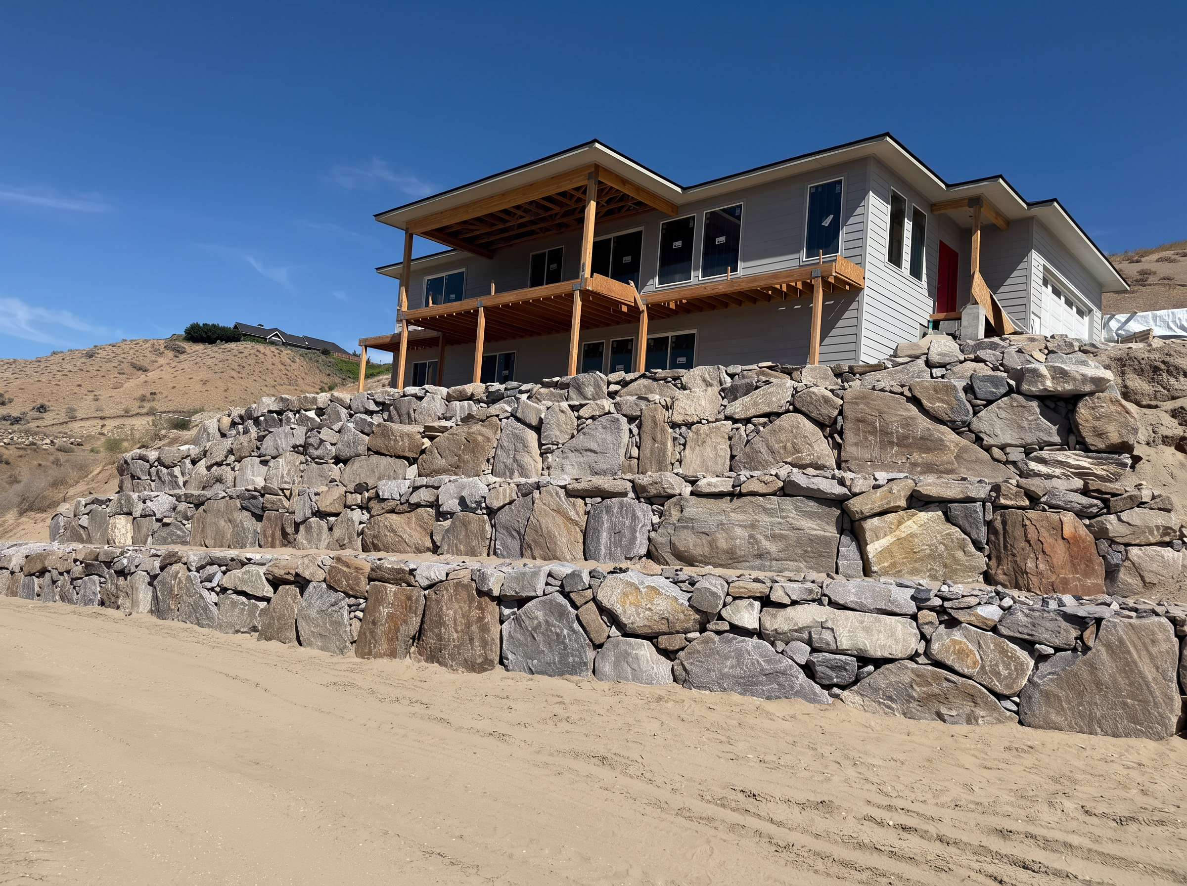 Natural rock retaining wall supporting a new hillside home